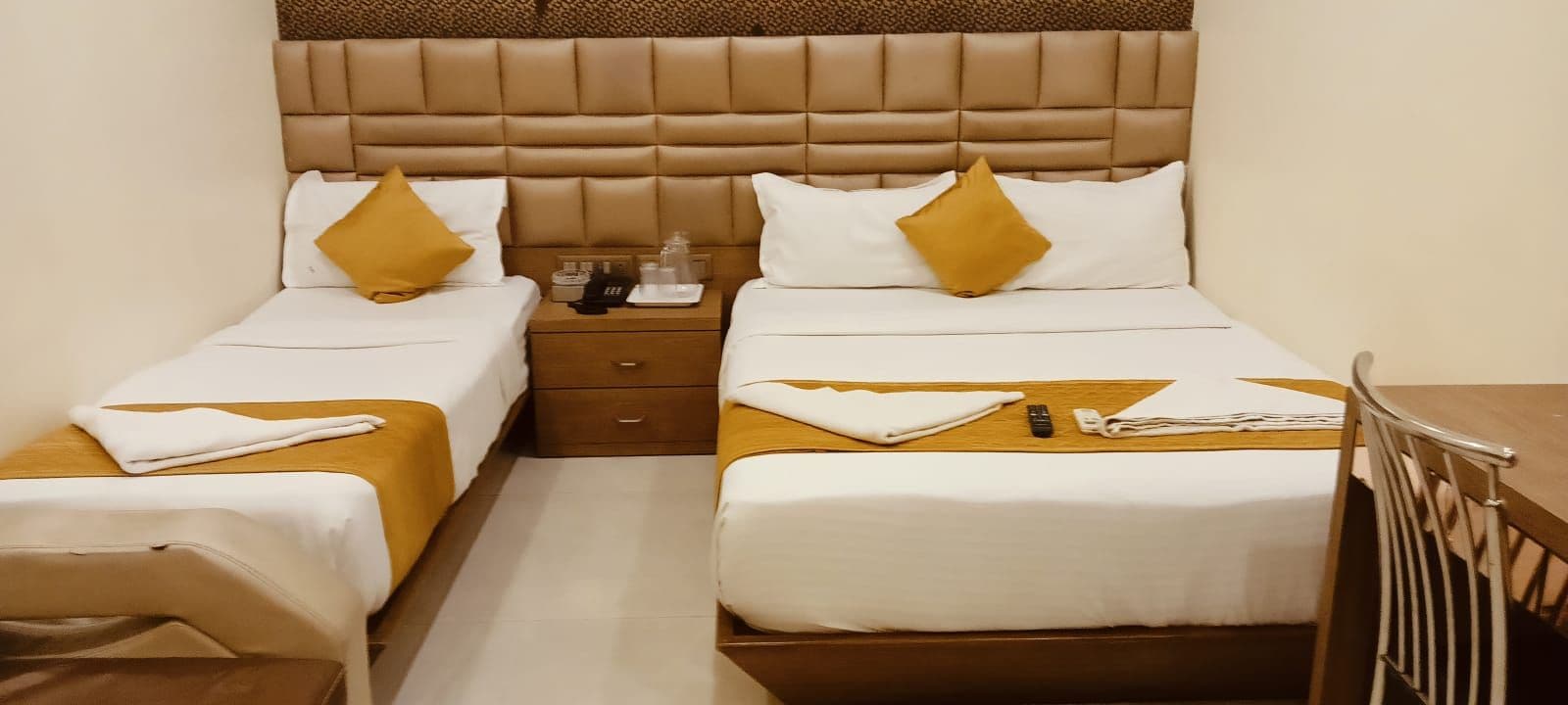 A hotel room with two beds, a wooden nightstand, and a small table.