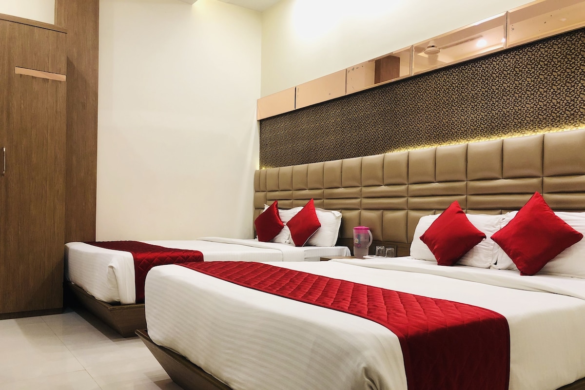 A hotel room with two beds, a wooden wardrobe, a headboard with a textured pattern, and a wall-mounted shelf.