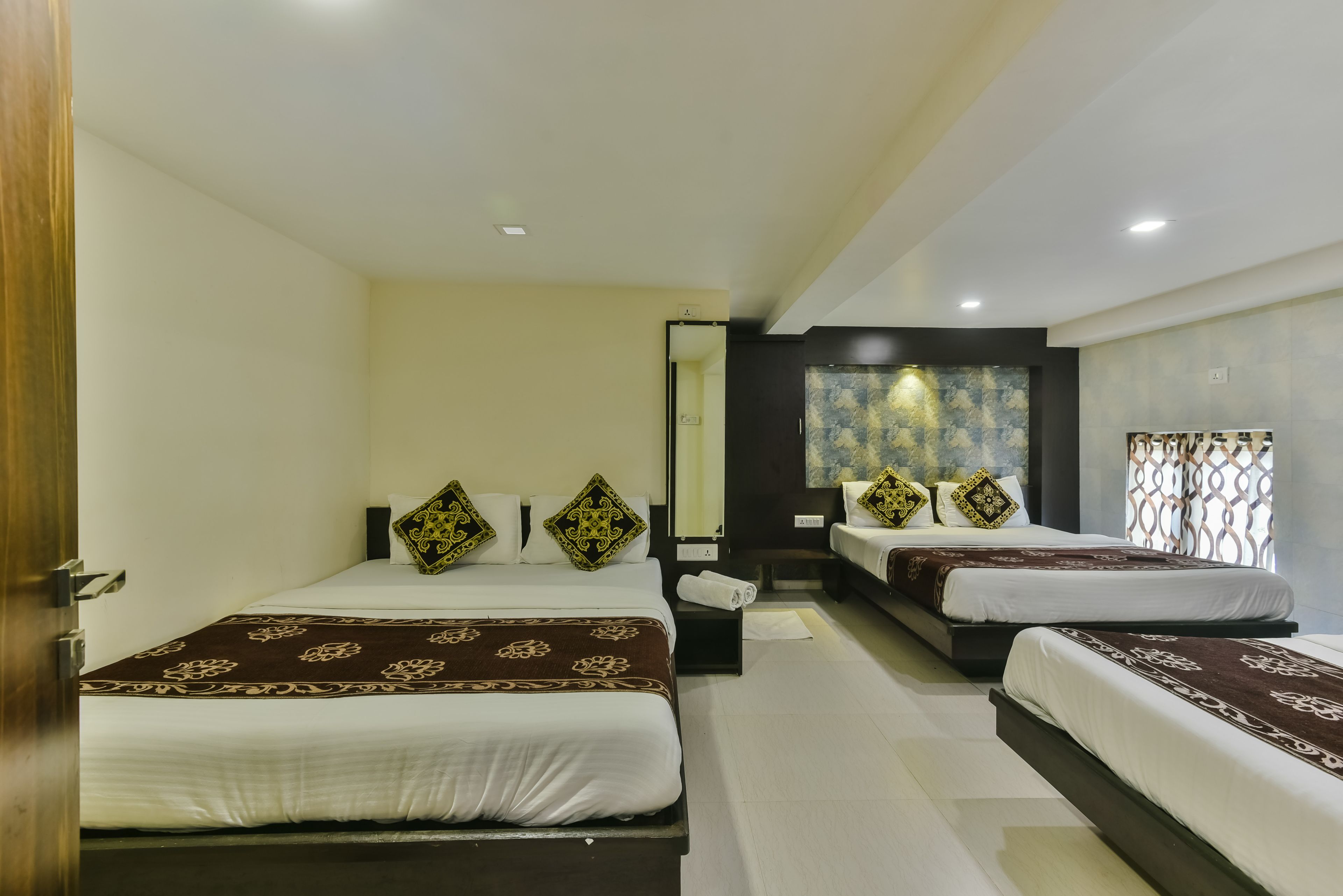 A hotel room with two beds, each with patterned bedspreads and decorative pillows.