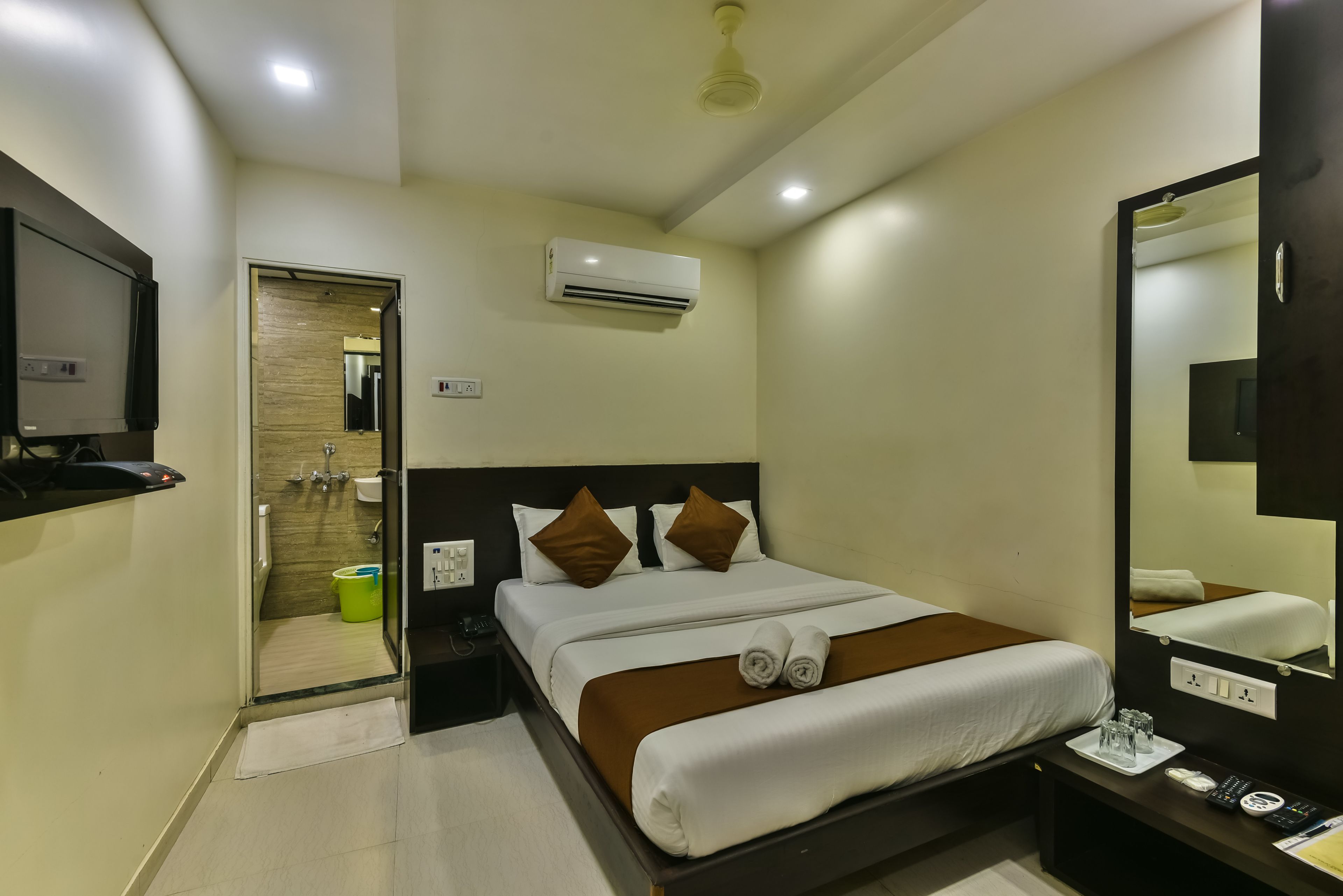 Een hotelkamer met een bed, nachtkastje, spiegel en een airconditioning.