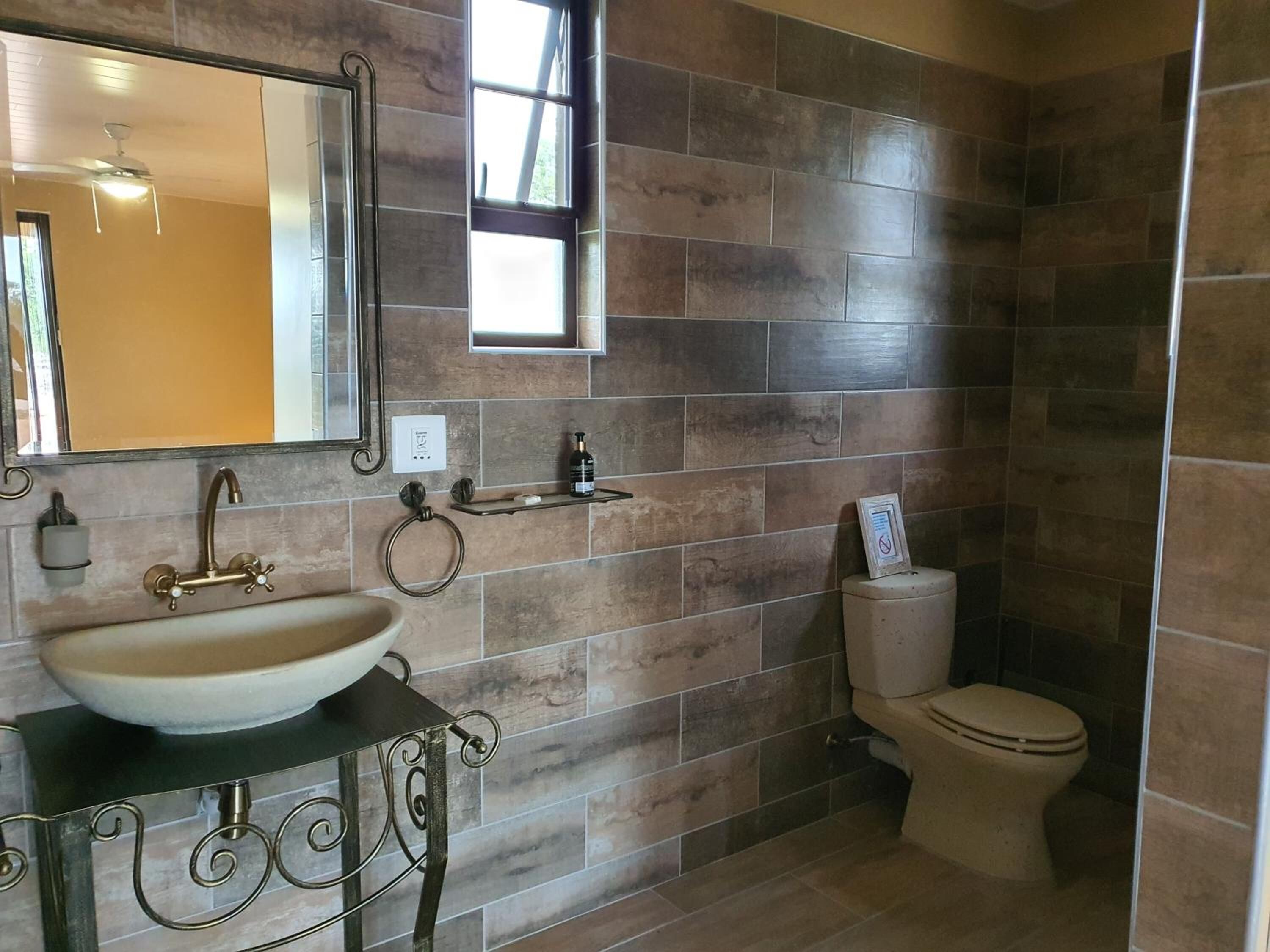 A bathroom with a large mirror, a vessel sink, a toilet, and a shower area.