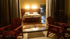 A bedroom with a large bed, wooden headboard, two chairs, and a fur rug. - Callies Game Lodge Safaris (Tsumeb)