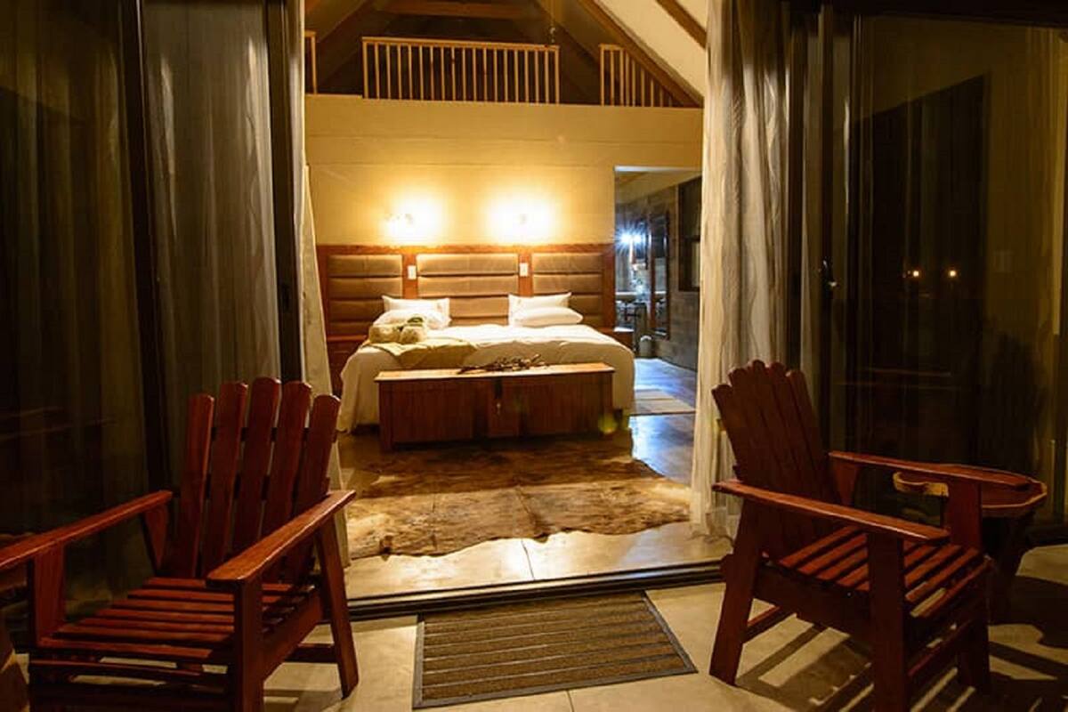 Un dormitorio con una cama grande, cabecera de madera, dos sillas y una alfombra de piel.