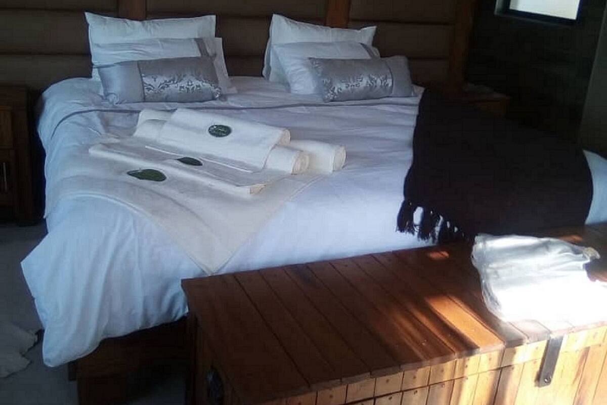 Una cama bien tendida con sábanas y almohadas blancas, un cabecero de madera y una mesita de noche de madera con una lámpara.