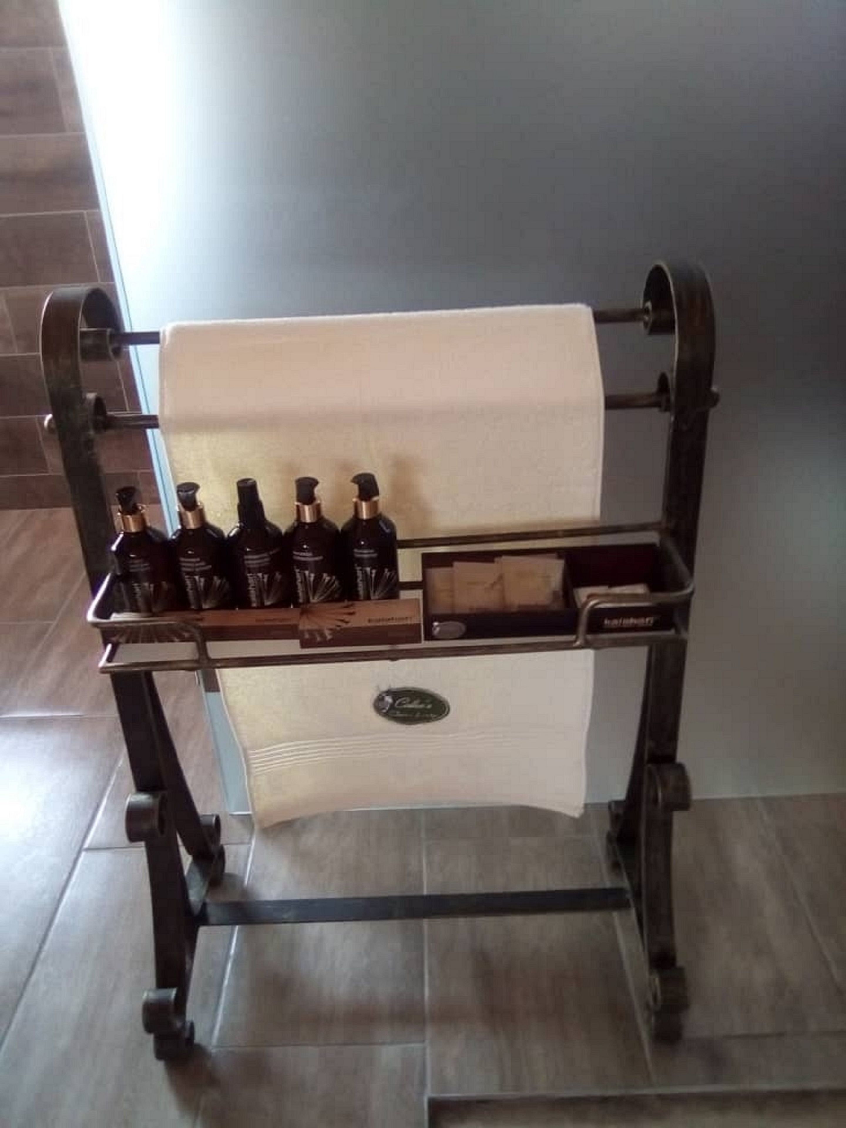 A metal cart with a white cloth, holding several dark bottles, likely containing toiletries.