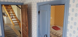 Una habitación con una escalera de madera que lleva a una zona superior, una cama con edredón estampado y una puerta con marco azul.