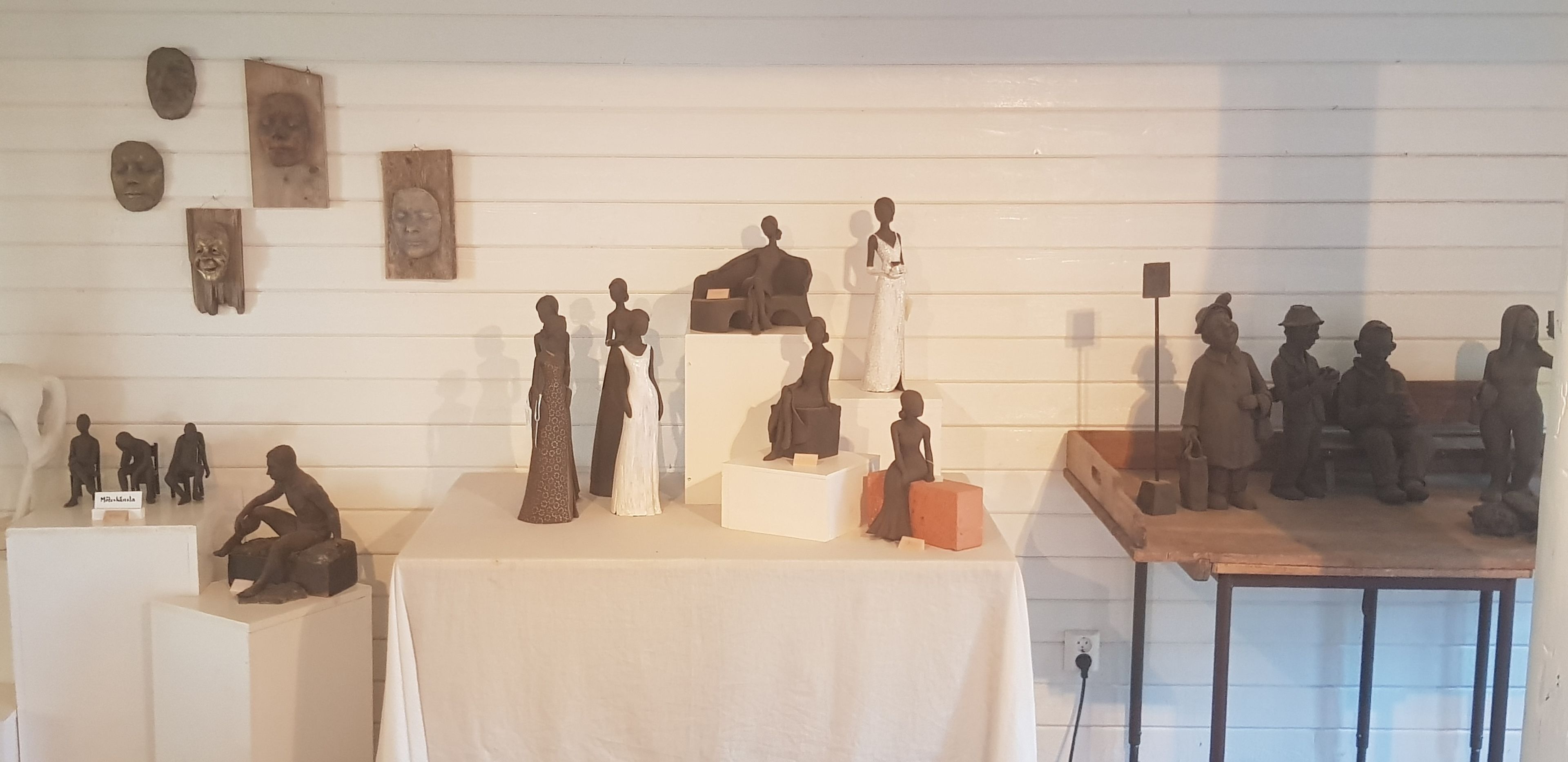 Verschillende sculpturen staan op een tafel voor een witte muur.
