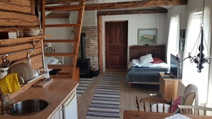 A rustic room with a wooden kitchen, a bed with a blue blanket, and a wooden chair. - Nygården Bed&Breakfast (Harmanger)