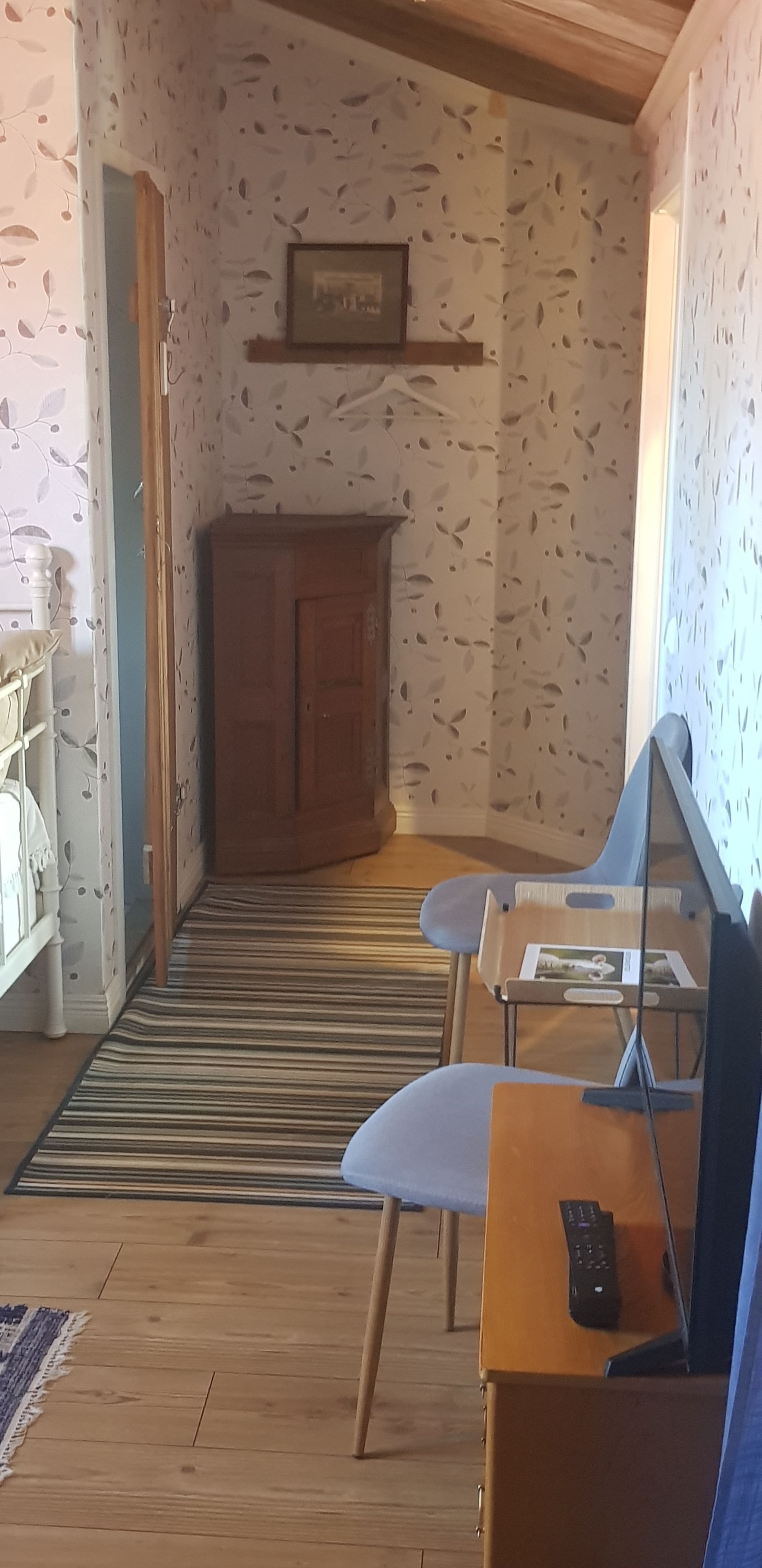 A room with a wooden floor, a striped rug, a blue chair, a small table with a remote control, and a cabinet.