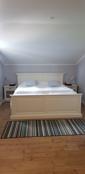 Un dormitorio con una cama grande, cabecera blanca, dos mesitas de noche y una alfombra a rayas.