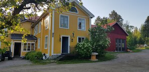 Una casa amarilla con puerta azul, un granero rojo y un árbol en primer plano.