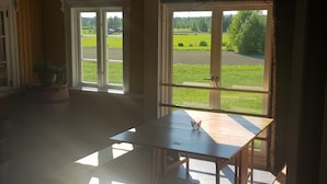 A room with a large window, a wooden table, and a cabinet with glass doors. - Nygården Bed&Breakfast (Harmanger)
