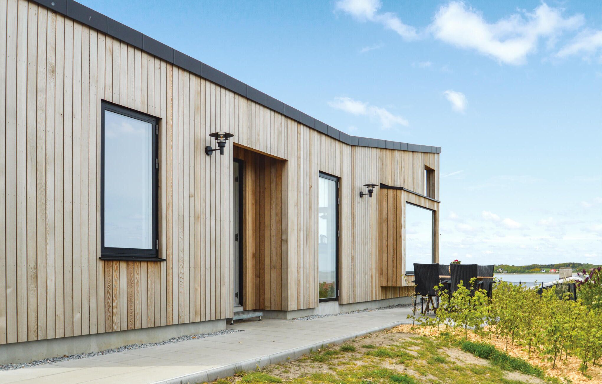 A modern wooden building with large windows and a patio area with outdoor seating.
