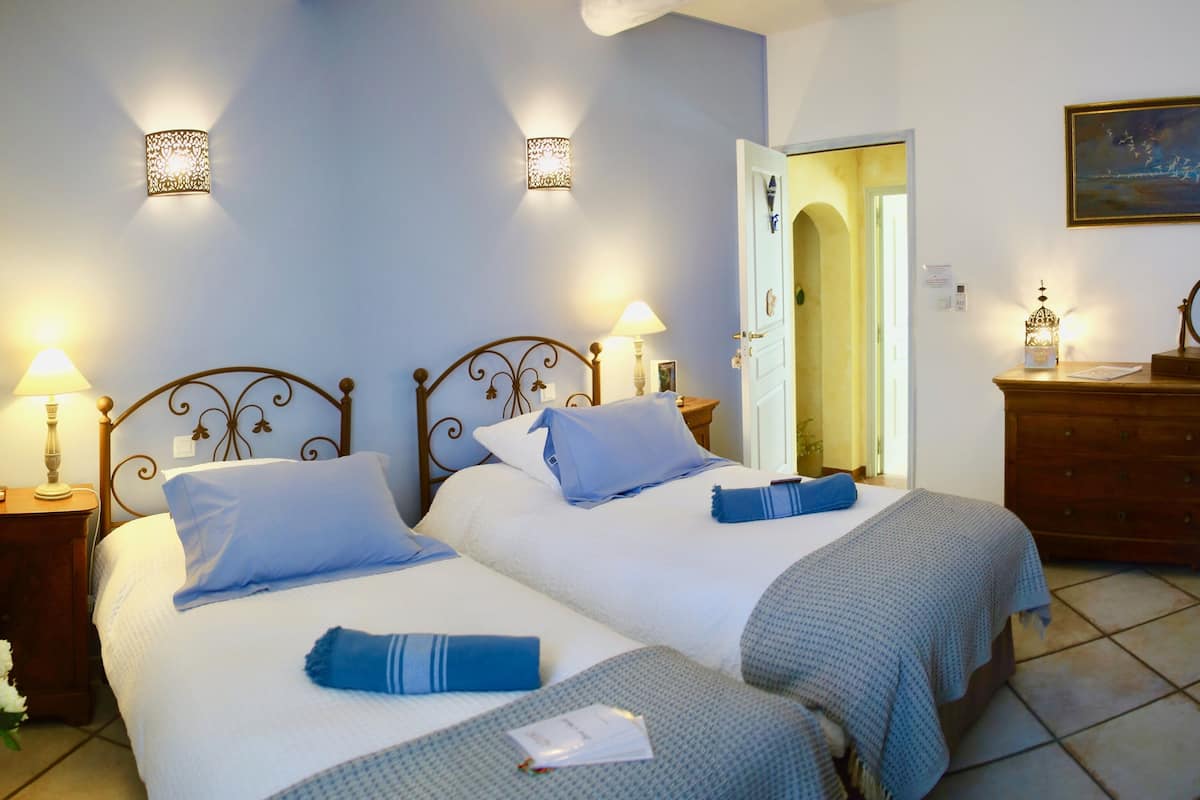 Habitación de hotel con dos camas, lámparas de noche, un aparador y un cuadro en la pared.