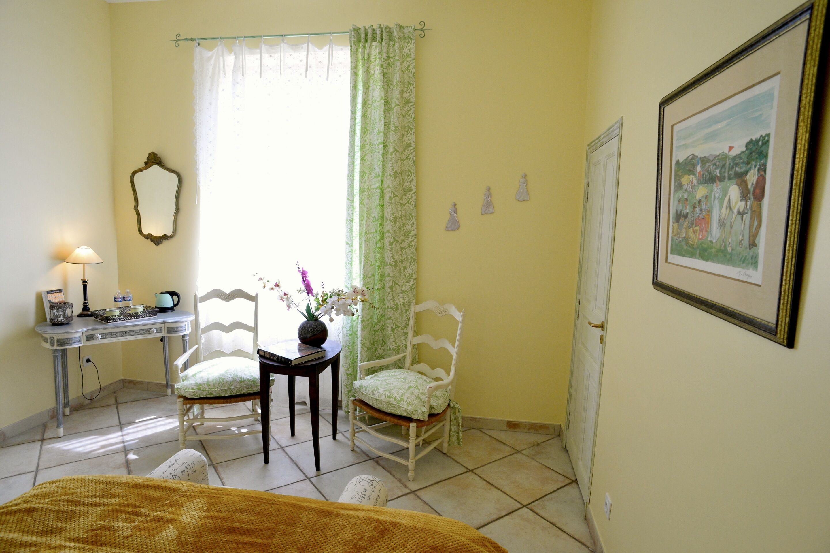 Un dormitorio con cama, escritorio con lámpara, silla, ventana con cortinas e imagen enmarcada en la pared.