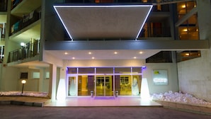 Een moderne hotelentree met een glazen gevel, een centrale ingang en een bord dat het een parkhotel aanduidt.