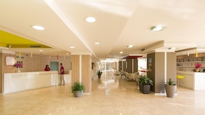 Een ruime lobby met een receptiebalie, zithoek en potplanten.