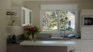 Une cuisine moderne avec des meubles blancs, un îlot central intégré, un vase de fleurs et une vue sur l’extérieur.