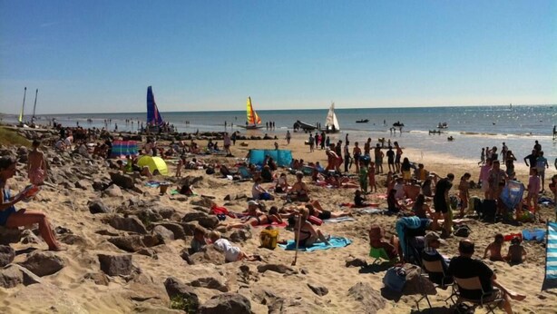 Une plage bondée où les gens se prélassent au soleil et se baignent.