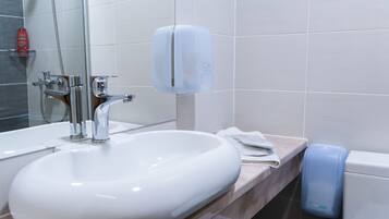 Un baño con lavamanos blanco, espejo, dispensador de jabón de mano y dispensador de toallas.