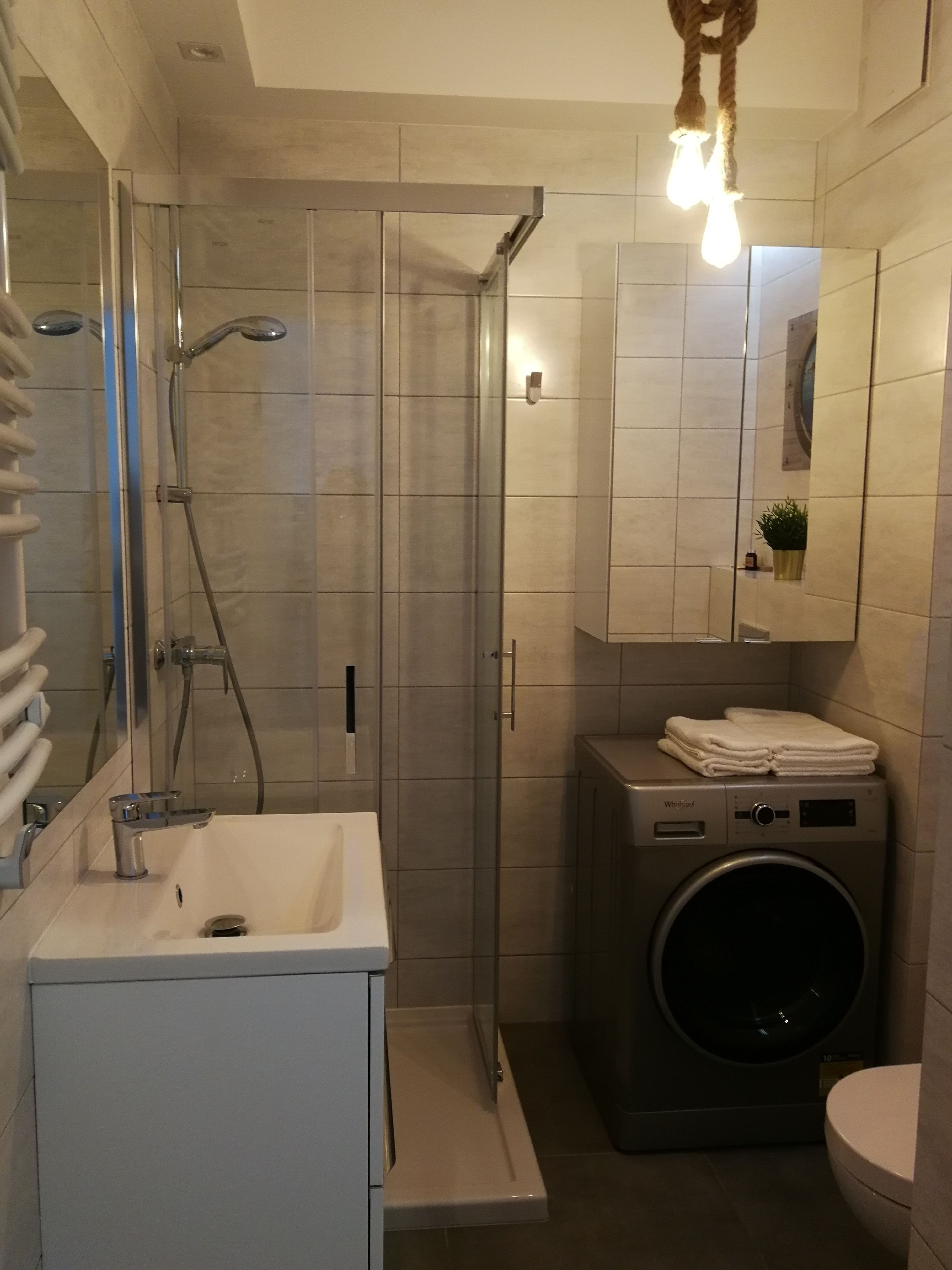 Ein modernes Badezimmer mit Duschkabine, integriertem Waschbecken, Waschmaschine und Toilette.