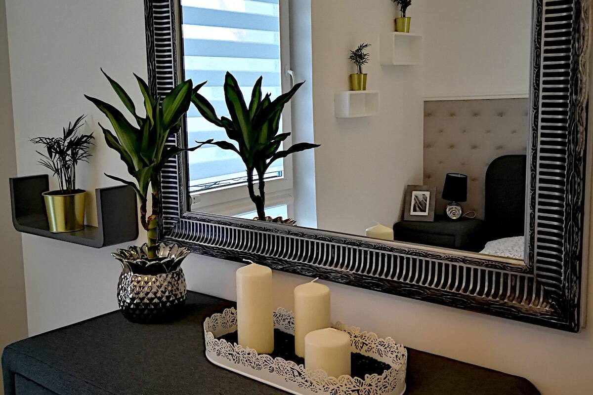 A room with a dark-colored dresser, a mirror with a decorative frame, and two potted plants.