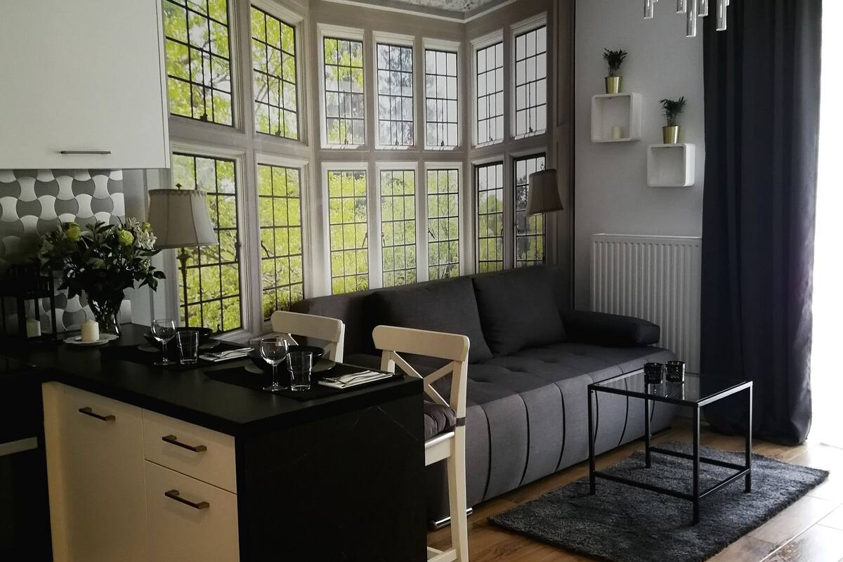 A modern kitchen with a central island, a dining area with a sofa, and large windows with a view of greenery.