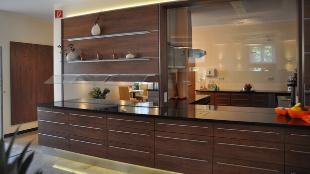 Eine moderne Küche mit Holzausstattung, einer Glasrückwand und einem Einbauherd.