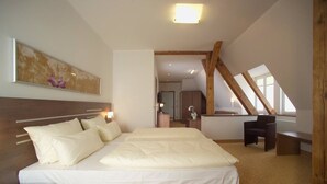 Ein Schlafzimmer mit einem großen Bett, einem Holz-Kopfstück, einem Nachttisch, einem Schreibtisch und einem Stuhl. Es gibt ein Fenster mit Blick nach draußen.