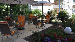 Eine Außenpatio mit Tischen und Stühlen, umgeben von einem Garten mit verschiedenen Blumen und einer Zierkugel.