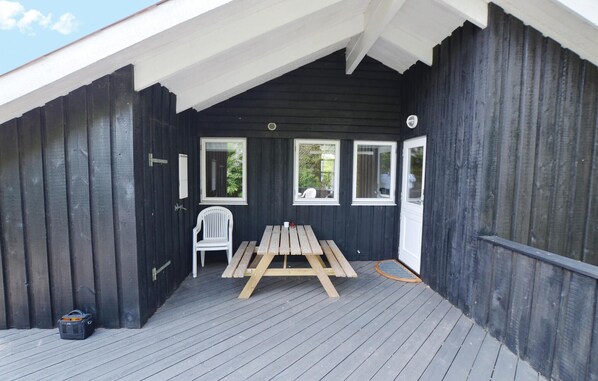 Un espace extérieur abrité avec une table et des chaises en bois, une chaise blanche et un sac noir posé sur le sol.