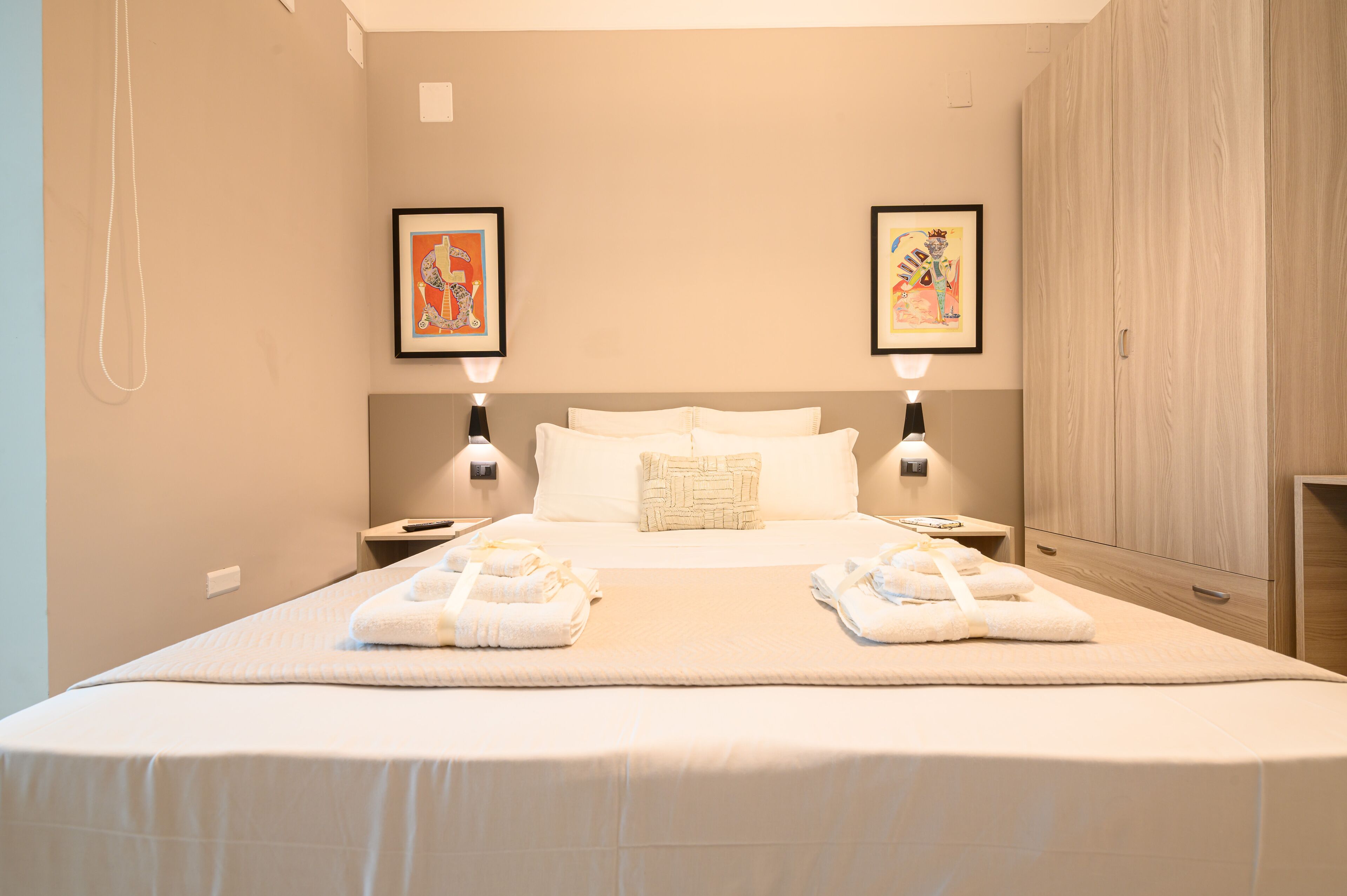 Een hotelkamer met een groot bed, twee nachtkastjes, een garderobe en twee ingelijste foto's aan de muur.