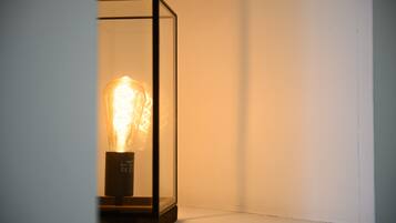 A light bulb encased in a clear glass box with a black base, placed against a plain wall.