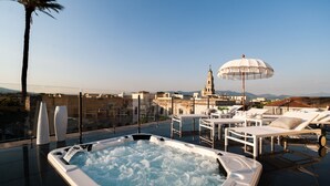 Una terraza en la azotea con un jacuzzi, sillones de descanso y un paraguas blanco.
