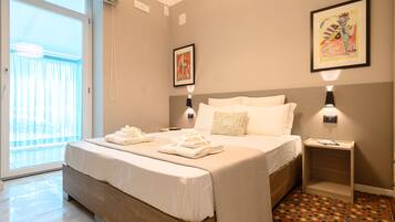 Una habitación de hotel moderna con una cama grande, una mesita de noche pequeña, un velador, una ventana con cortinas y dos lámparas de pared.