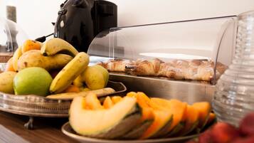 Un buffet de petit-déjeuner proposant des fruits, des viennoiseries et une machine à café.