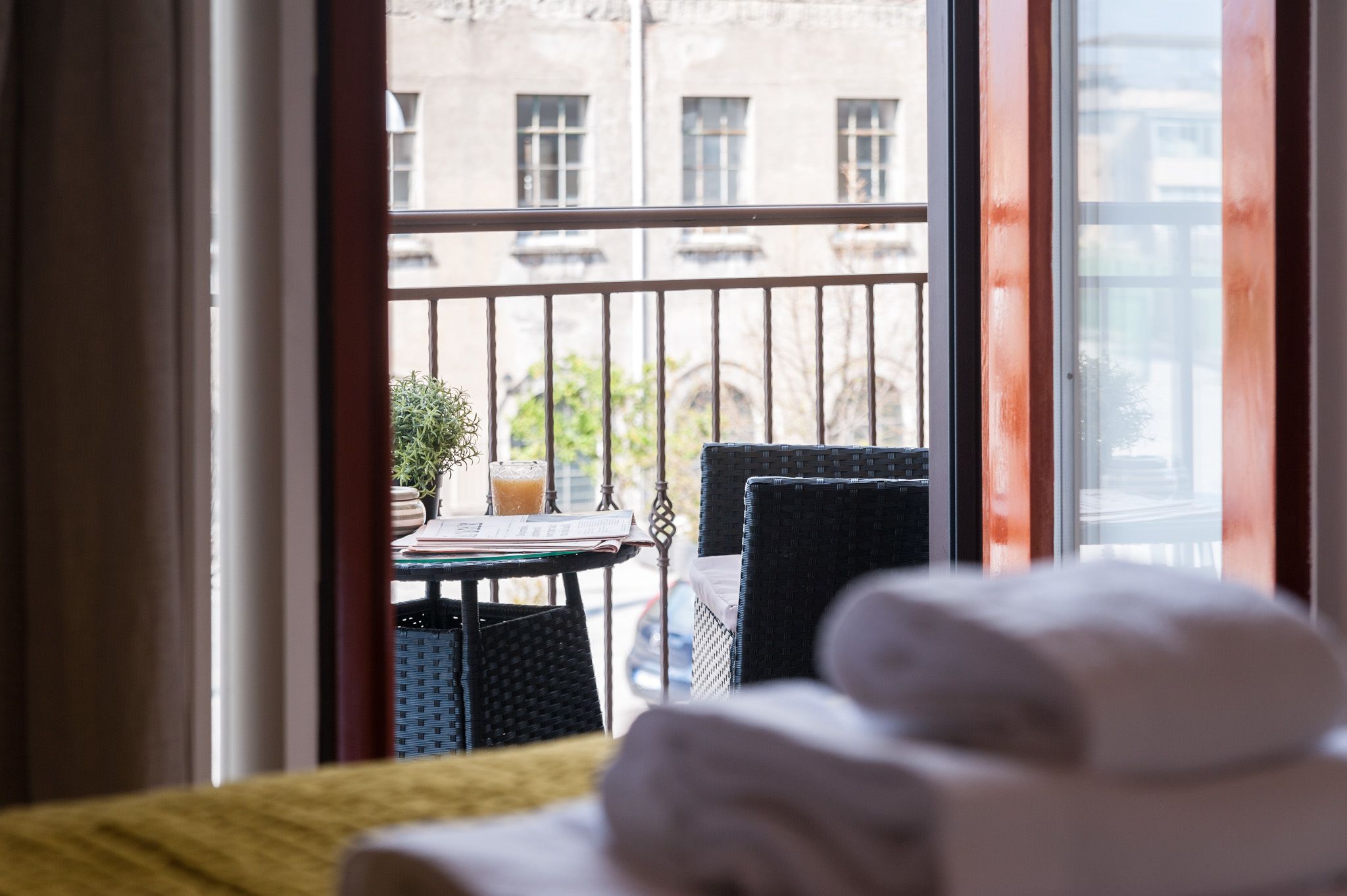 A hotel room with a balcony, a table with a glass of orange juice, and a chair.