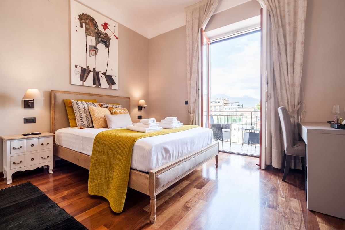 Quarto com cama, mesas de cabeceira, escrivaninha e varanda com vista.