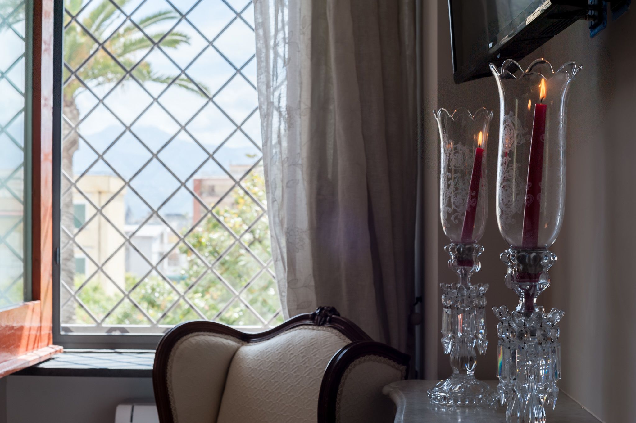 A room with a window, a chair, and three lit candles on a table.