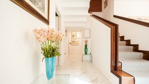 Un pasillo con una escalera, un jarrón azul con flores y cuadros en las paredes.