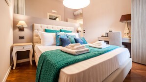 Una cama bien hecha con una manta verde, una mesita de noche con una lámpara y un escritorio con una lámpara.