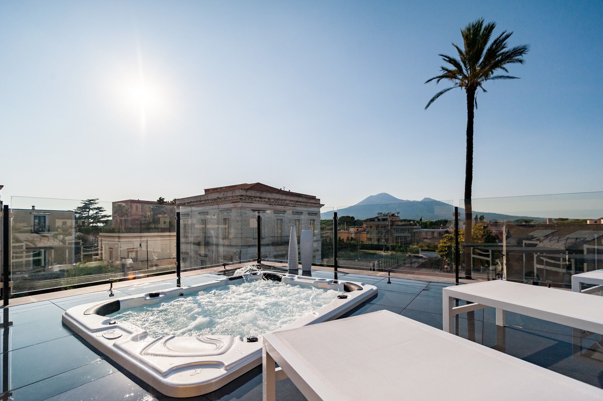 A rooftop terrace with a hot tub, lounge chairs, and a view of buildings and mountains.