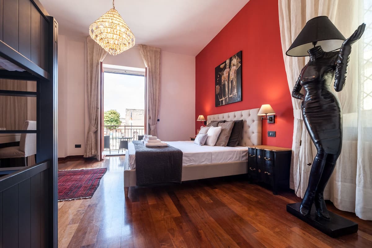 Quarto com parede vermelha, uma cama grande, um candelabro e um manequim.
