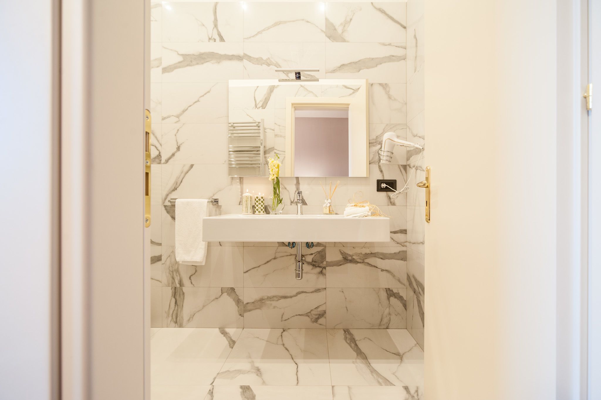 A bathroom with a marble wall, a sink, a mirror, and a towel rack.