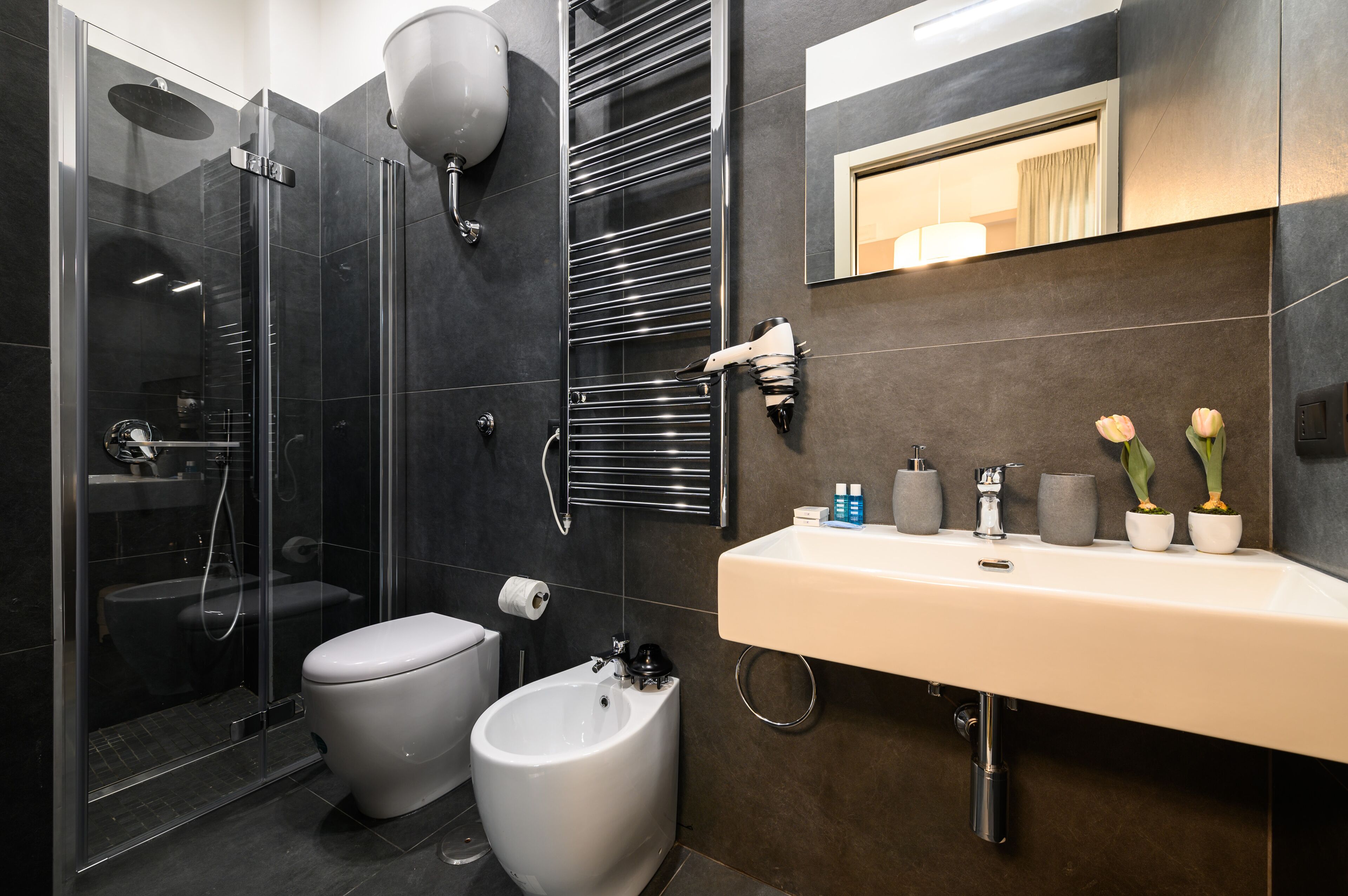 A modern bathroom with a glass-enclosed shower, a bidet, a toilet, and a sink with toiletries.