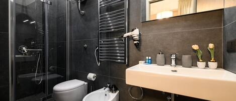 A modern bathroom with a glass-enclosed shower, a bidet, a toilet, and a sink with toiletries.