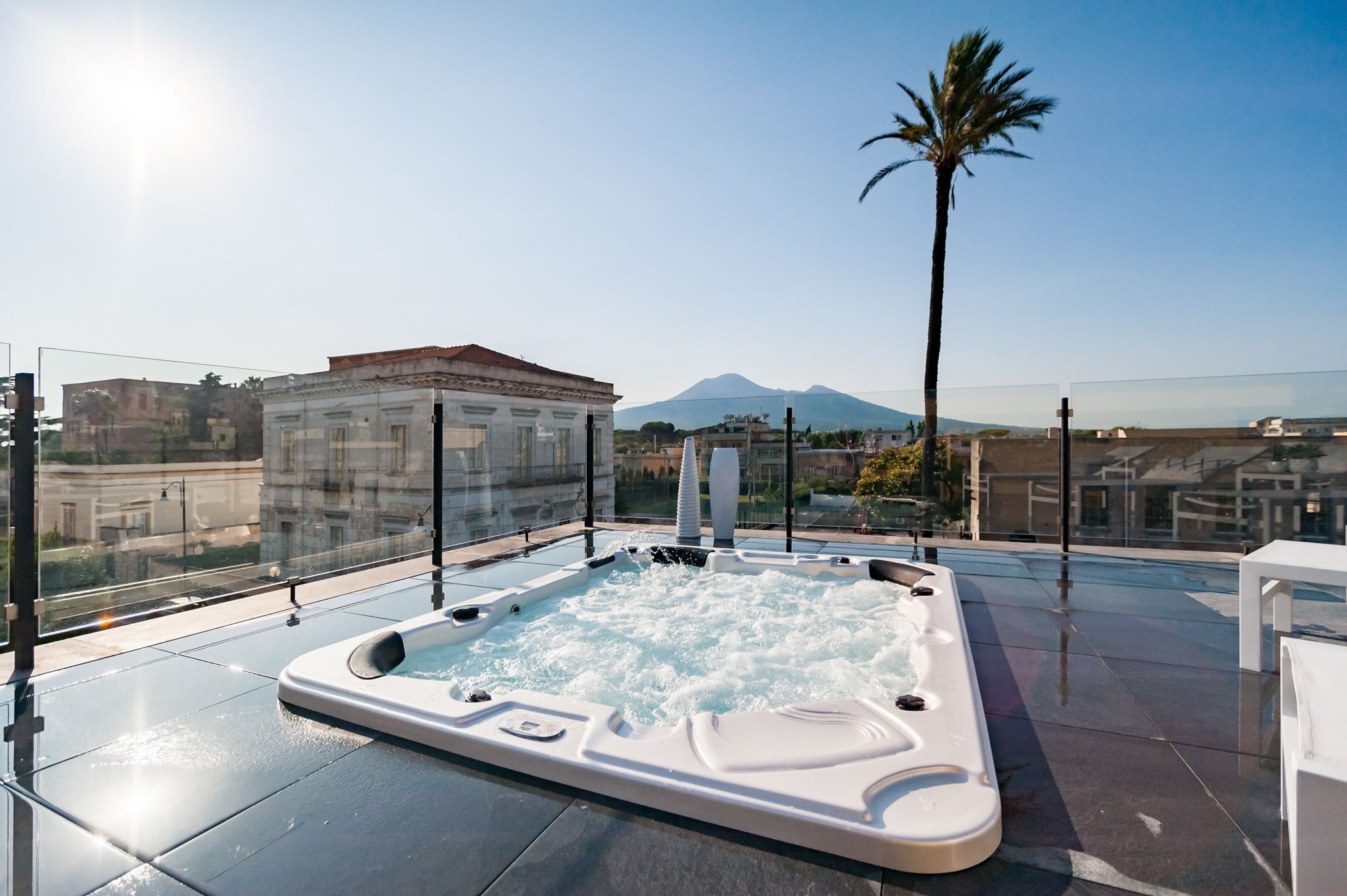 A rooftop jacuzzi with a mountain view, surrounded by glass railings and modern architecture.