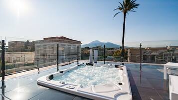 A rooftop jacuzzi with a mountain view, surrounded by glass railings and modern architecture.