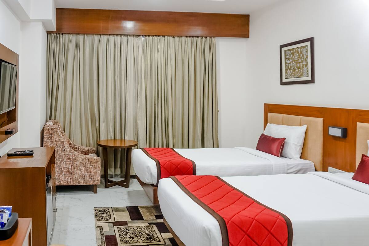 A hotel room with two beds, a TV, a desk, a chair, and a curtain.