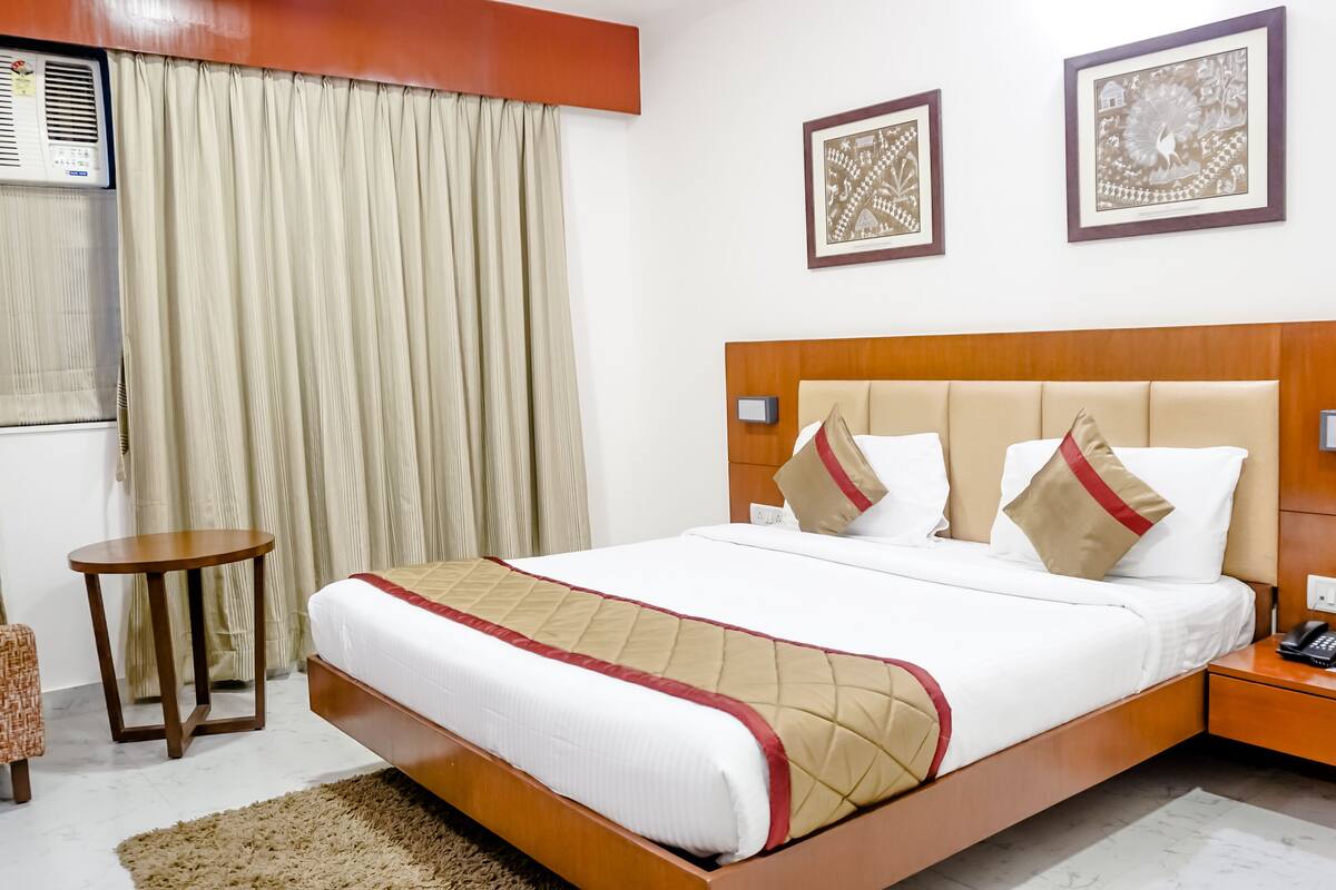 A hotel room with a large bed, bedside tables, a small round table, and two framed artworks on the wall.